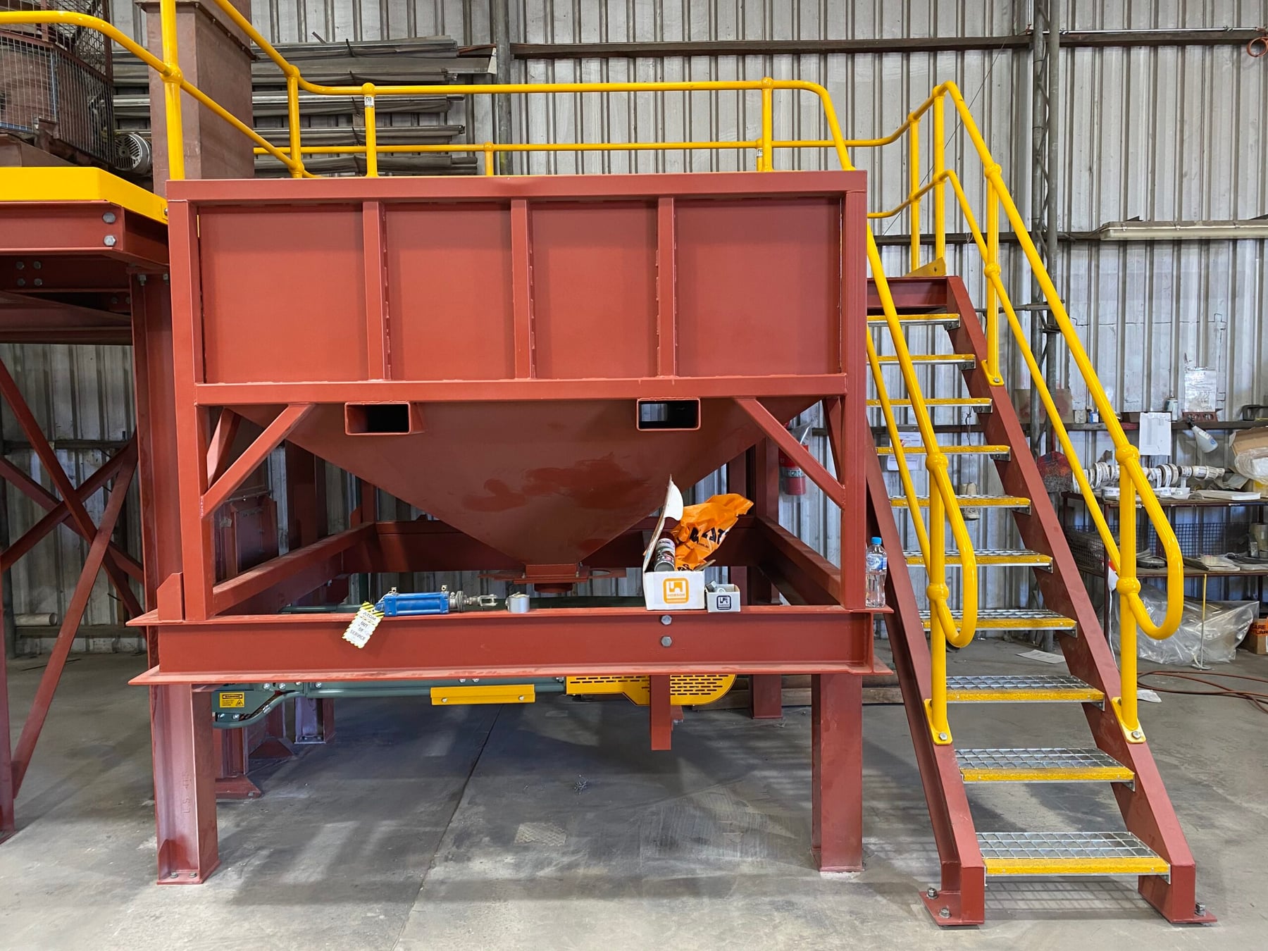 Red oxide painted surge bin with access stairs and yellow handrails in the Twomeys workshop